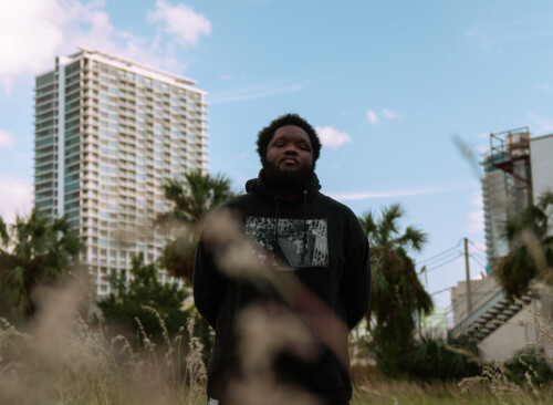 Wahid standing in a field in front of tall buildings